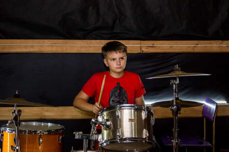 a young drummer plays drums, cymbals with sticks, sitting on a special chairの写真素材