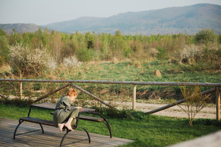 Young red-haired woman sitting on a bench in the park.の写真素材