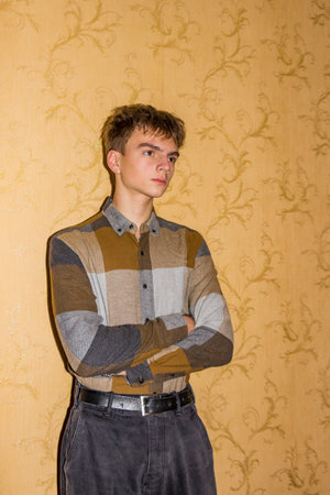 guy standing near orange wall, profile, brunette teenager, brown eyes, looking up, original hairstyle, arms crossed on chest, plaid shirt, black jeans, student, young manの写真素材