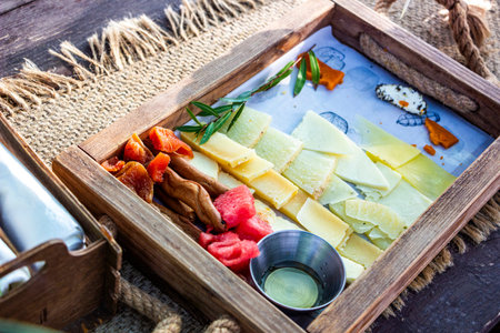wooden board with different cheeses, assortment of cheeses, snacks, colors, textures, several types, red watermelon, fruits, vegetables, breadsticks, greens, bowl of honeyの写真素材