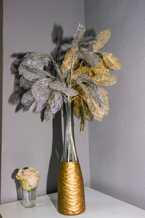 Decorative leaves on branches with silver shiny coating in vase with narrow neck, metallic gold, real rose in stack, openwork, gold paint, painted vesselの写真素材