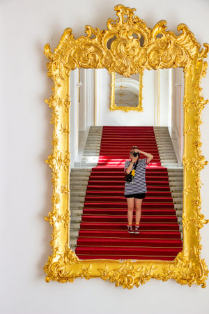 teenager girl in striped T-shirt, taking a picture of herself in the mirror on the stairs, gold...