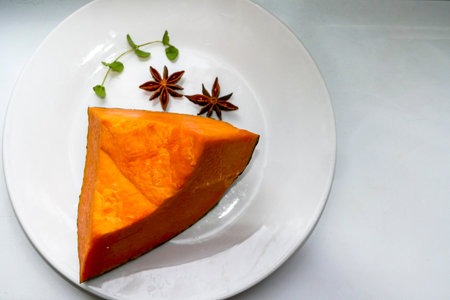 piece of pumpkin on white plate, pumpkin fruit, orange vegetable, sprig of mint, microgreens, close-up, rich color, inner pulp, fresh, healthy foodの写真素材