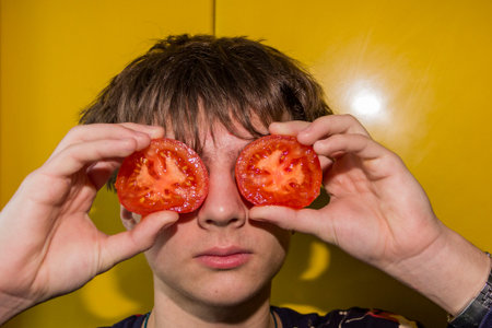 beautiful teenager holds halves of tomatoes as glasses, rich pink color, juicy, healthy eatingの写真素材