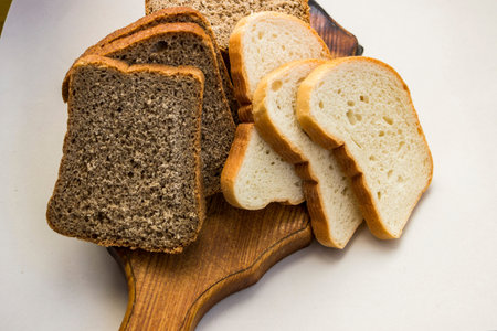 slices of bread of different types, stacked on a wooden board, white, rye, part of the dark,