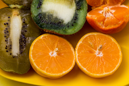 yellow plate with tropical fruits cut in half, macro, green kiwi, pink orange, tangerine, healthy eating, fortified food, breakfast,の写真素材