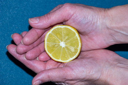 yellow half of lemon in woman's palms, hands holding citrus, useful, daylight, close-up, food, vitamins, blue backgroundの写真素材