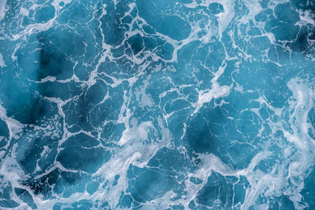 Rough deep turquoise and blue sea with white foam bubbles texture backgroundの写真素材