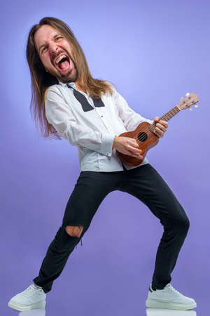 male singer sings to the guitar ukulele, stands on a purple backgroundの写真素材