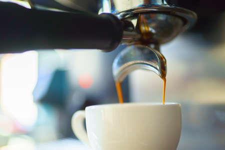 espresso coffee is pouring from the coffee machine into a white cup