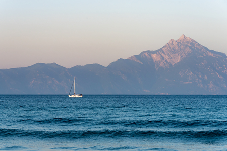 Lonely boat sailing at sunset on a calm sea, Mount Athos in the backgroundの写真素材