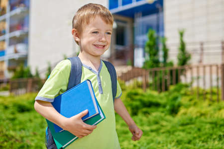 Young happy boy with books in front of school buildingの写真素材