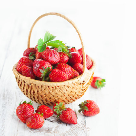 Fresh strawberries in a wicker basket on a white wooden background.の写真素材