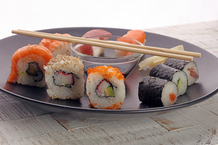 Sushi rolls on a black plate with chopsticks on white backgroundの写真素材