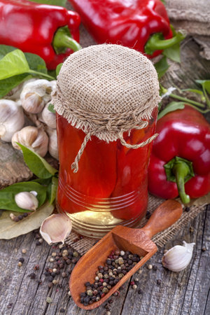 Pickled red peppers in a glass jar and spices on wooden backgroundの写真素材