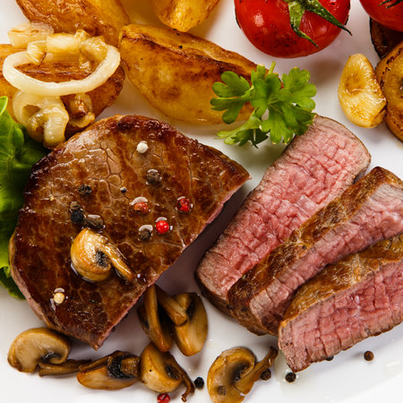Grilled beef steak with mushrooms and vegetables on a white background.の写真素材