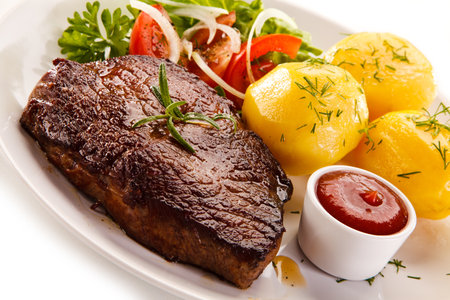 Grilled steak with potatoes and salad on a white background in a restaurantの写真素材