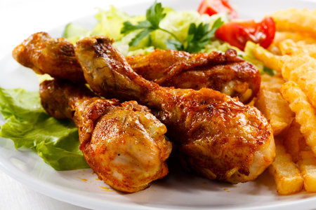 Grilled Chicken Legs with French Fries and Vegetables on White Plateの写真素材