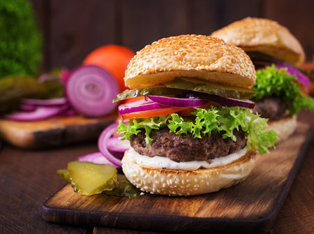 Big sandwich - hamburger burger with beef, pickles, tomato and tartar sauce on wooden background.の写真素材