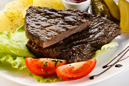 Grilled beef steak with vegetables and sauce on white plate closeupの写真素材