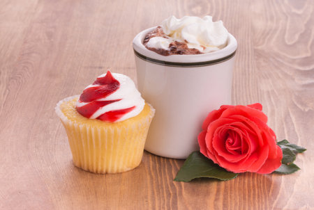 Strawberry cupcake with a cup of hot chocolate and a bright red rose on dark wooden tabletop - anniversary or Valentine's treat to a loved oneの写真素材