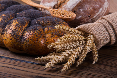 Bread with poppy seeds and wheat ears on a wooden background.の写真素材