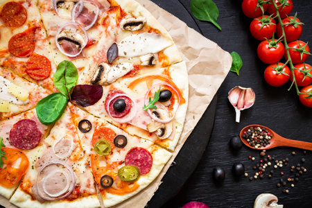 pizza with salami, olives and tomatoes on a black backgroundの写真素材