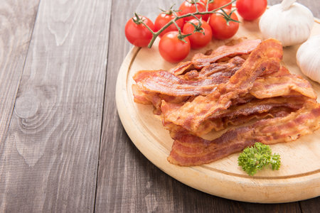 Fried bacon, tomato and garlic on the wooden board.の写真素材