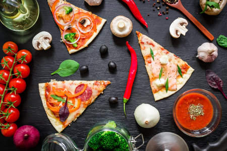 Slices of pizza and ingredients on black wooden background, top viewの写真素材