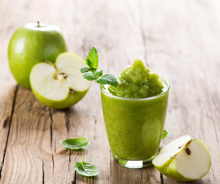 Glass of apple puree with a fresh apple decorated with leaves of mint on a rustic wooden background with copy space.の写真素材