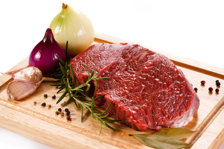 Raw beef steak with rosemary, garlic and pepper on wooden boardの写真素材