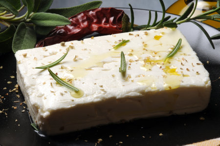 Feta cheese with rosemary and spices on a black plate.の写真素材