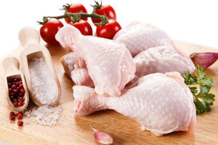 Raw chicken legs with spices and vegetables on a wooden board. Isolated on white background.の写真素材
