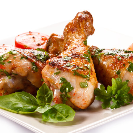 Grilled chicken legs with tomato and parsley on a white plateの写真素材