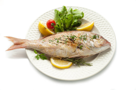 Grilled fish with lemon and herbs on a white plate on a white backgroundの写真素材