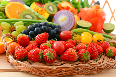 Fresh fruits and vegetables in a wicker basket on a wooden tableの写真素材