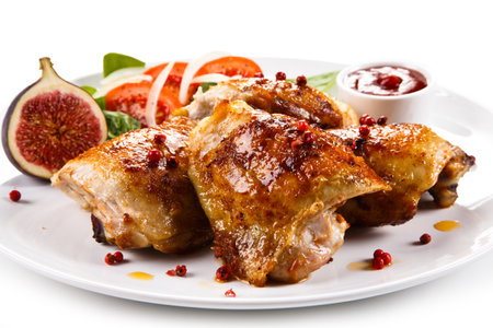 Roast chicken legs with vegetables and sauce on a white background.の写真素材