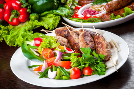 Grilled sausages on skewers served with fresh vegetables and greensの写真素材