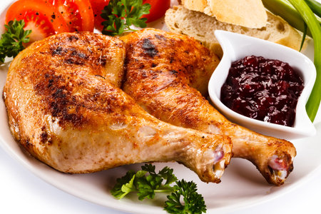 Roast chicken legs with vegetables and cranberry sauce on white backgroundの写真素材