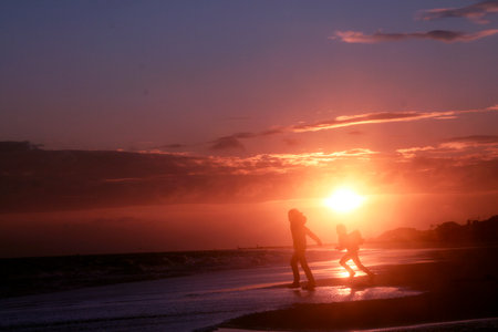 Silhouette of a mother and son walking on the beach at sunsetのeditorial素材