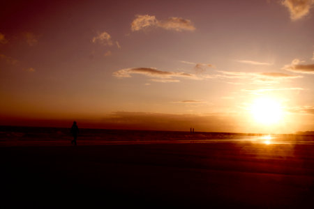 Silhouette of a man walking on the beach at sunset.のeditorial素材