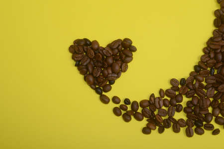Coffee beans in heart shape on yellow backgroundの写真素材