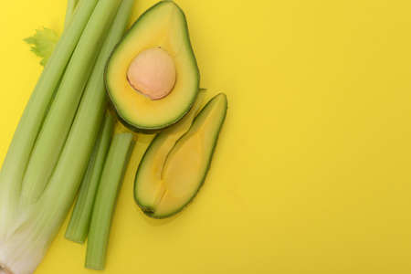 A half of avocado and celery sticks on an yellow background. Space for text, copy space. Vegetarian...