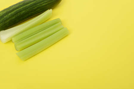 Celery stalks and cucumber in the corner isolated on yellow background. Space for text, copy space. Vegetarian backgroundの写真素材