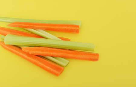 Fresh green celery and carrots on yellow background. Space for text, copy space. Vegetarian backgroundの写真素材