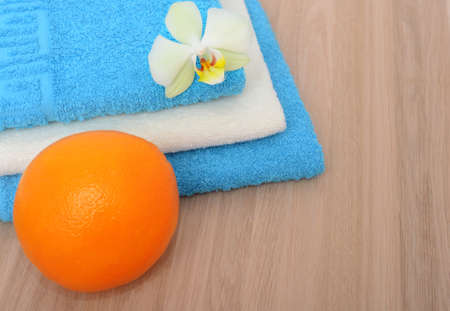 Blue and white stacked bathroom towels, orange and orchid flower on a woden backgroundの写真素材