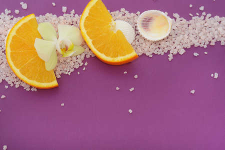 Seashells, sliced orange and orchid flower on seasalt over purple background. Copyspace.の写真素材