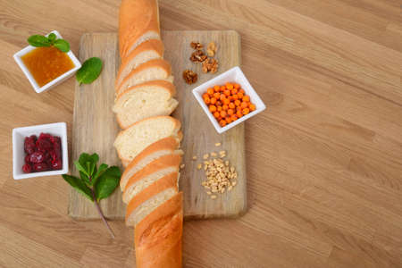 Sliced baguette on a cutting board and three bowls of jam on wooden table. Top view.の写真素材