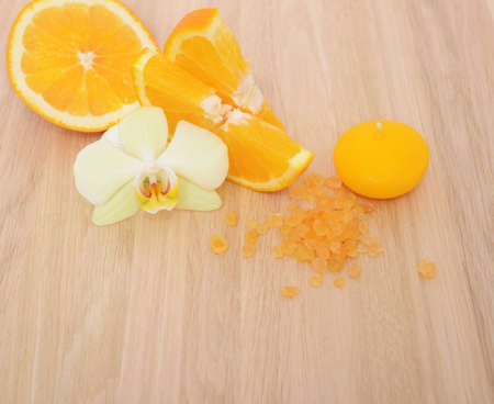 Flower of orchid on orange slices, aroma salt and yellow candle on wooden table backgroundの写真素材