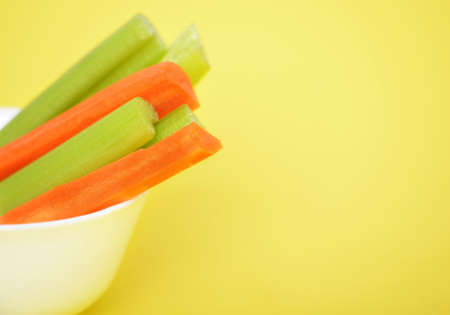 Fresh green celery and carrots on yellow backgroundの写真素材
